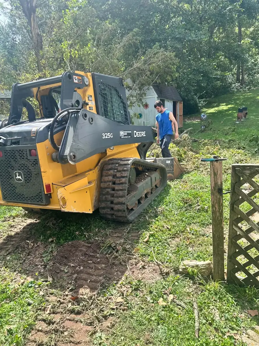 Jake from MJB Landscaping clearing storm-damaged branches with a John Deere 325G